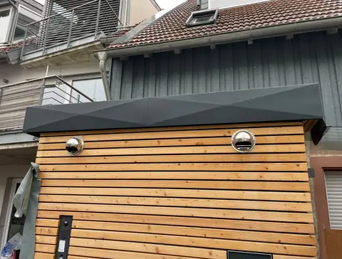 Vordach mit Blechabdeckung im Rautenmuster über einer Holzfassade